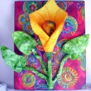 Lily - 16" x 20" Three dimensional design of a lily done in yellow to orange ombre fabric. Background is a Ricky Timms colorful print fabric.